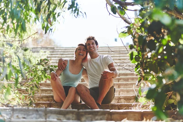 Casal feliz sentado nas escadas do lado de fora olhando para longe — Fotografia de Stock