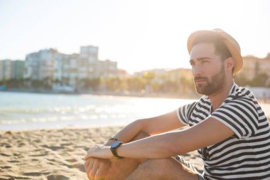 Şapka uzakta plaj seyir oturan genç dalgın adam