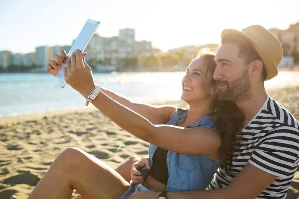 Mulher feliz tomando selfie com seu namorado por tablet na praia — Fotografia de Stock