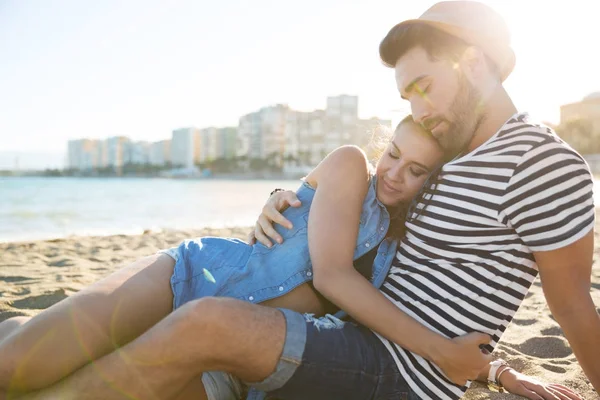 Jovem casal feliz sentado na praia abraçando — Fotografia de Stock
