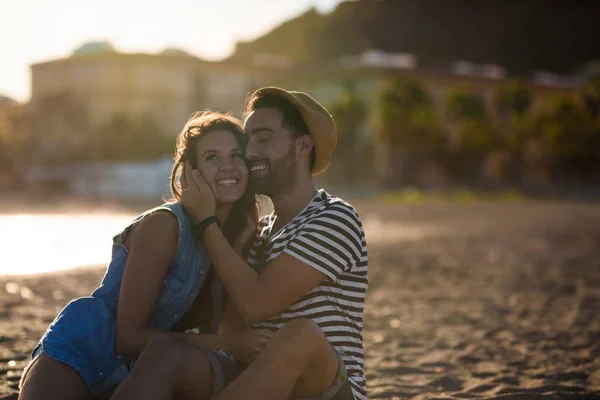 Pareja feliz sentados juntos en la playa riendo —  Fotos de Stock