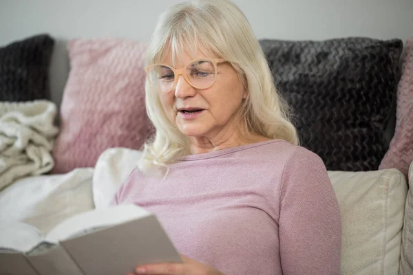 Senior senhora em casa ler livro atentamente — Fotografia de Stock