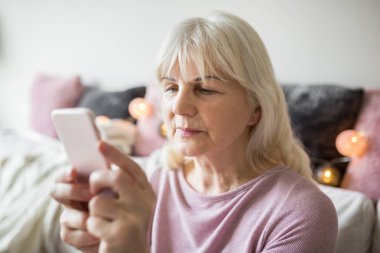 Üst düzey kadın evde oturan smartphone kullanarak