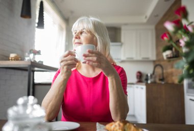 Kahve sahip mutfak masasına oturan memnun üst düzey Bayan