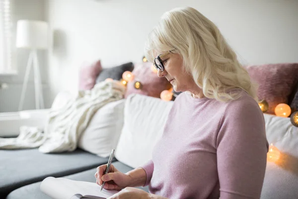 Señora mayor en gafas tomando notas en casa — Foto de Stock