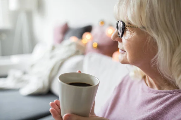 सेवानिवृत्त वरिष्ठ महिला कॉफी का कप पकड़े हुए दूर देख रही है — स्टॉक फ़ोटो, इमेज