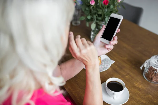 Senior dame met kopje koffie met smartphone — Stockfoto