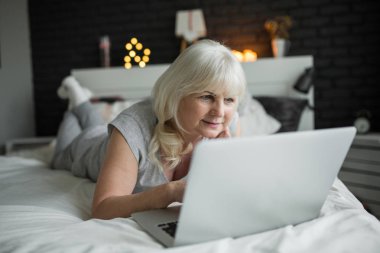 Dizüstü bilgisayar kullanarak yatakta yatarken memnun üst düzey Bayan