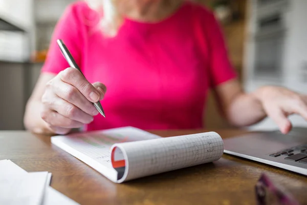 Seniorin, die zu Hause arbeitet und Notizen macht — Stockfoto