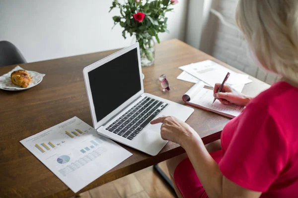 Senior dame werken bij keukentafel met behulp van laptop — Stockfoto