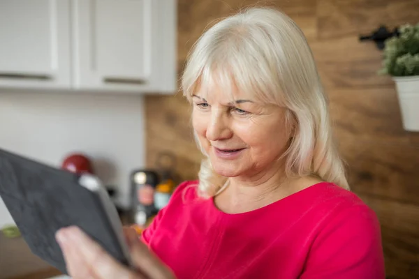 Feliz señora mayor en vestido rojo usando tableta en la cocina — Foto de Stock