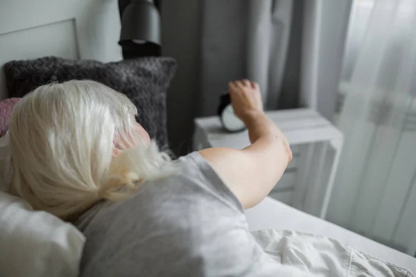 Senior Kobieta, leżąc w łóżku, wyłączanie budzika — Zdjęcie stockowe