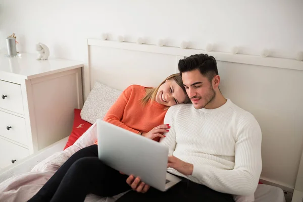 Pareja feliz sentada en la cama usando portátil — Foto de Stock