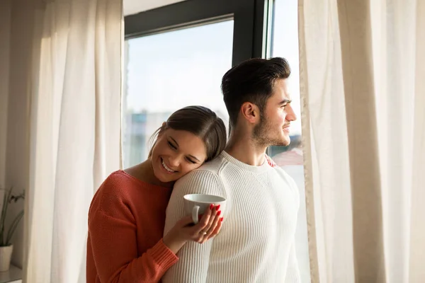 Счастливая женщина с чашкой кофе обнимается со своим парнем — стоковое фото