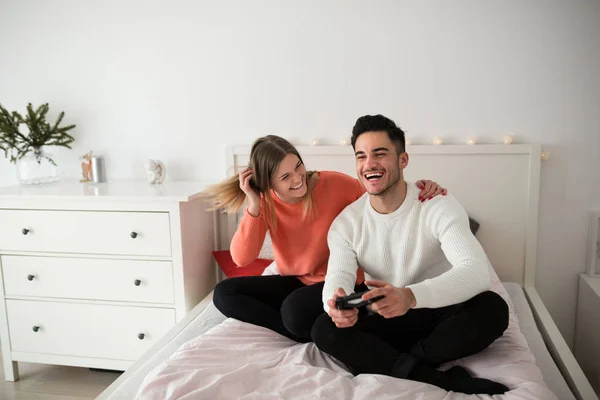 Mladý pár sedící na posteli hraje videohry směje — Stock fotografie