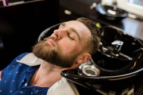 Молодой человек в парикмахерской ждет, чтобы вымыть волосы — стоковое фото