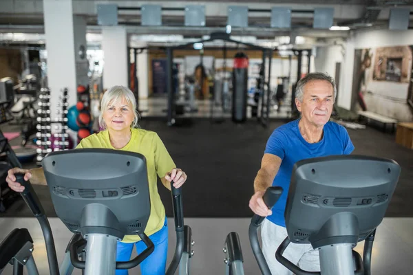 Glad senior people training on stair stepper at gym
