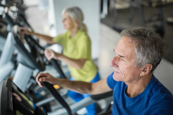 Senior man working out on stair stepper at gym