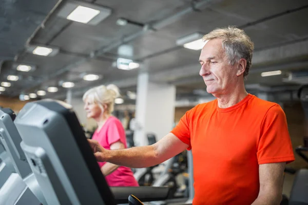 Senior mann som tar på skjermen til tredemølle i gymsalen – stockfoto