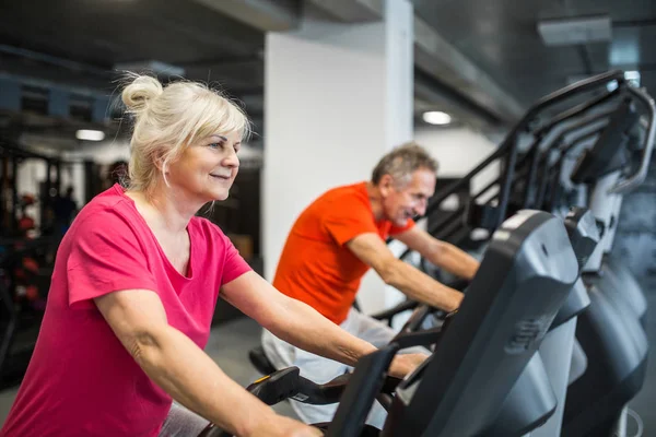 Feliz entrenamiento de la señora mayor en bicicleta de giro en el gimnasio — Foto de Stock