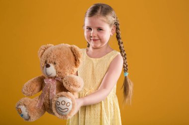 Oyuncak ayı tutarak sarı elbiseli genç mutlu kız