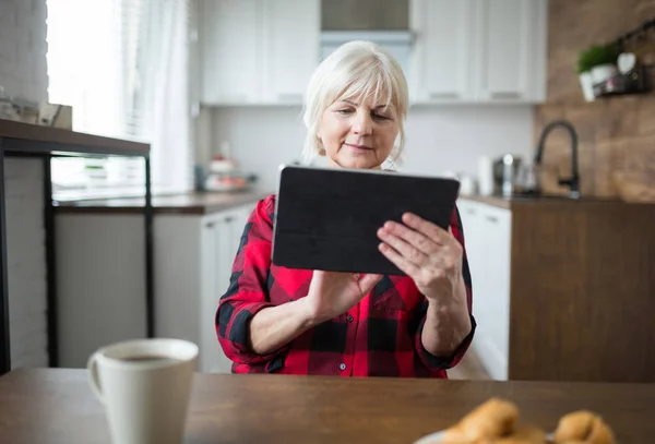 Señora mayor usando tableta en la mesa de la cocina — Foto de Stock