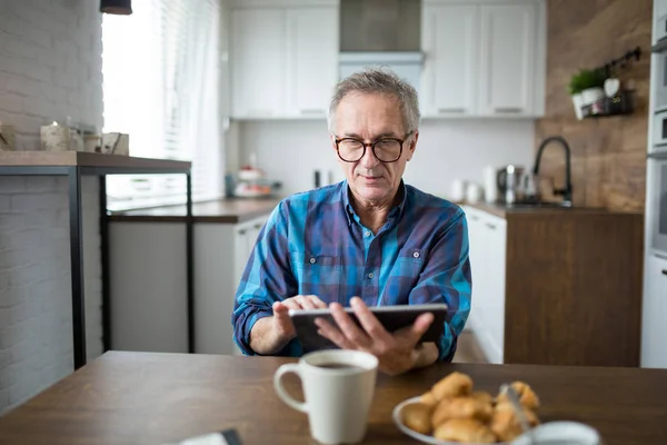 Homem sênior usando tablet na mesa da cozinha — Fotografia de Stock