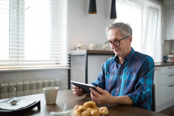Feliz homem sênior leitura ebook na cozinha — Fotografia de Stock