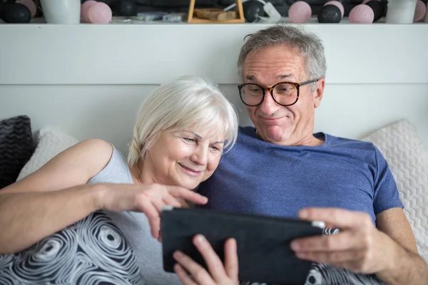 Feliz pareja de ancianos acostados en la cama usando tableta — Foto de Stock