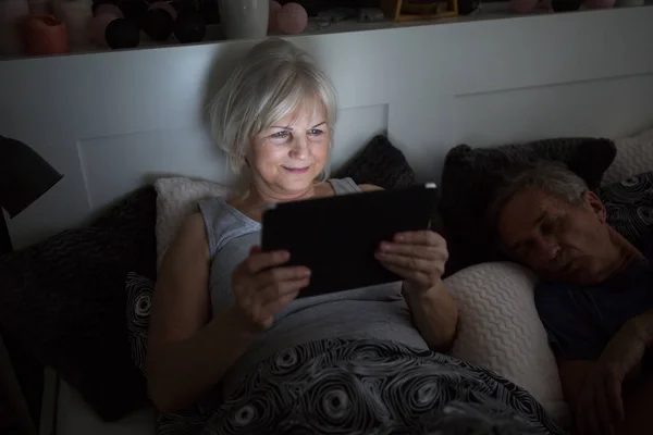 Feliz señora mayor acostada en la cama usando tableta — Foto de Stock