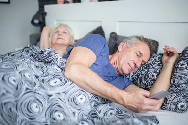 Hombre mayor acostado en la cama usando smartphone — Foto de Stock