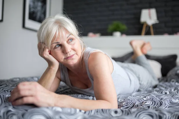 Senior pensive lady lying on bed looking away — Stock Photo, Image