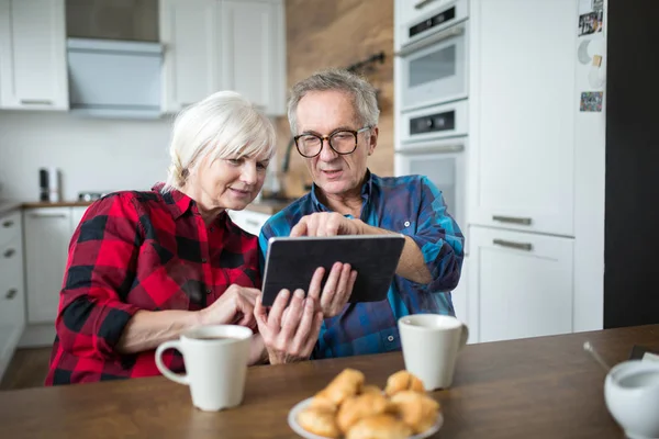 Casal sênior usando tablet na mesa da cozinha Imagens Royalty-Free