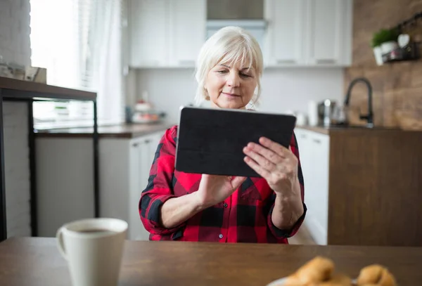 Senior dame met behulp van Tablet PC op de keukentafel Stockfoto