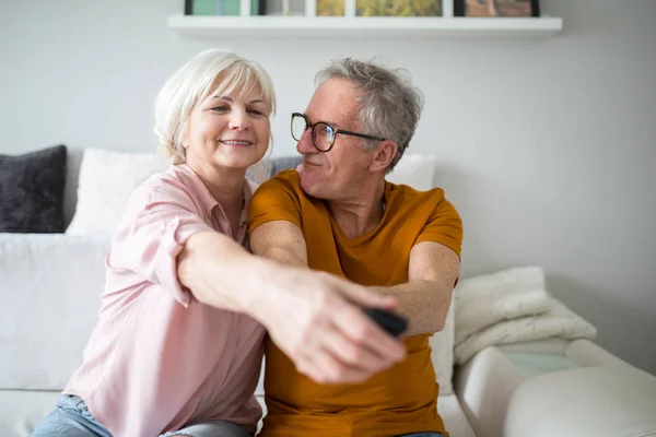 Gelukkige senior paar tv remote bij elkaar te houden Stockafbeelding