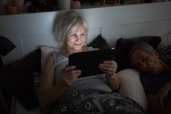 Щаслива старша леді лежить в ліжку за допомогою планшета Ліцензійні Стокові Фото