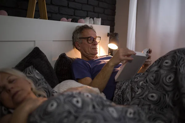 Senior man liggend in bed lezen boek Stockfoto