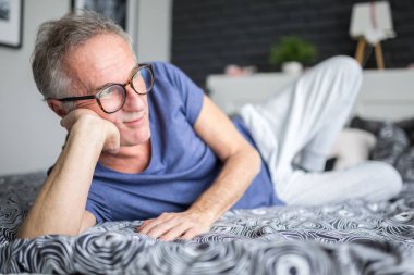 Senior man lying on bed thinking clipart