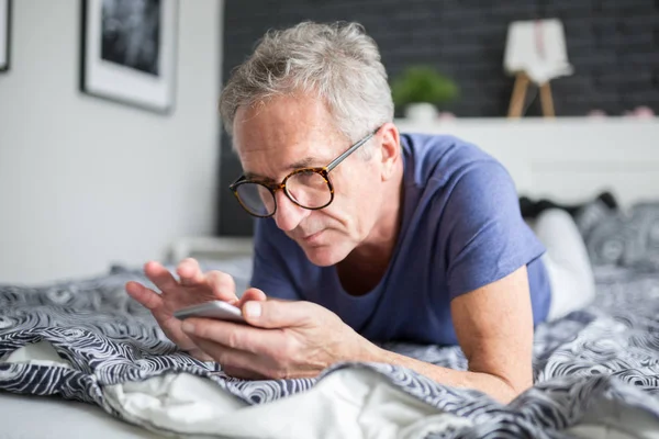 Hombre mayor acostado en la cama usando smartphone — Foto de Stock