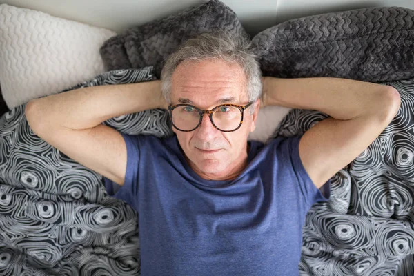 Feliz hombre mayor acostado en la cama pensando — Foto de Stock