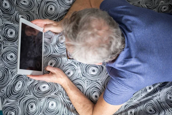 Homem idoso deitado na cama usando tablet — Fotografia de Stock