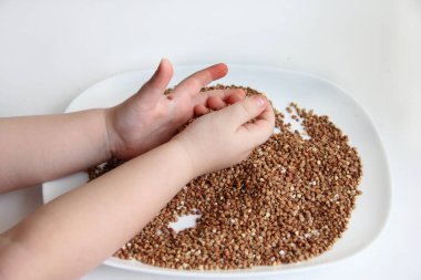 Çocuk karabuğday lapasıyla oynuyor. Çocuğun elleri ve lapası beyaz arka planda.