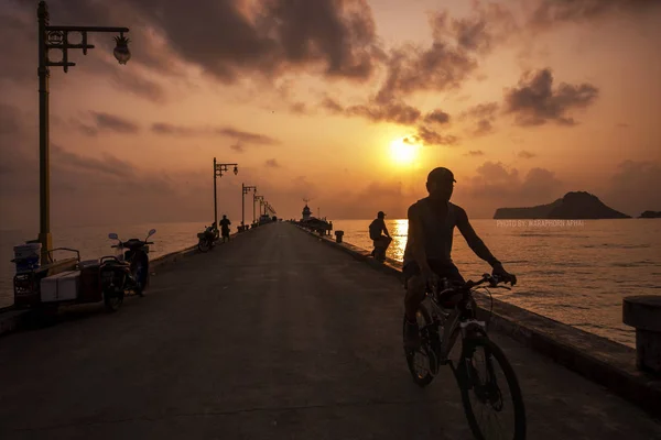 Silhouetted unidentified man riding a bike on jetty at Ao Manao bay in Prachuap Khiri Khan, Thailand