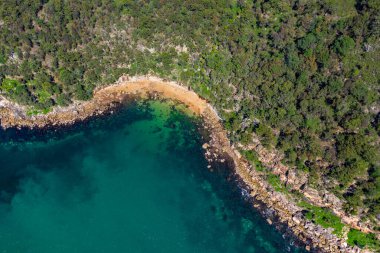 Ku-ring-gai Chase Ulusal Parkı 'nın kuzey kıyı şeridinin insansız hava aracı görüntüsü, yeşil ağaç ormanı ve yukarıdan alınmış turkuaz suyla kayalık sahil şeridi, kuş bakışı manzara.