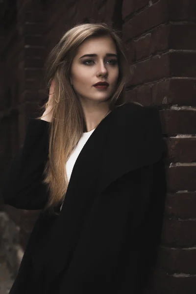 Mulher loira na moda em casaco quente perto de uma parede de tijolo — Fotografia de Stock