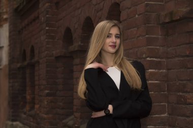 Bir tuğla duvar yakınındaki sıcak paltolu mutlu sarışın kadın