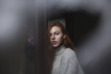 Beyaz perdenin arkasında çilli kızıl saçlı modelin portresi.