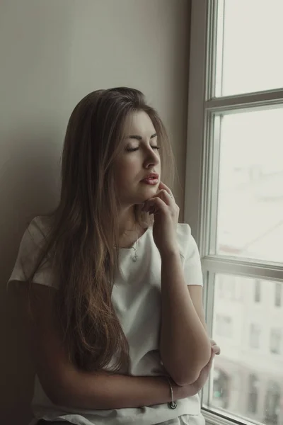 Wanita berambut cokelat muda yang lembut dengan blus putih di jendela — Stok Foto