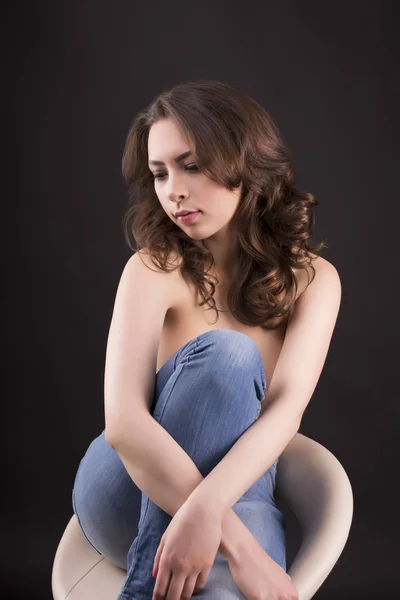 Mavi Jeans bir sandalyede oturan güzel üstsüz kadın — Stok fotoğraf