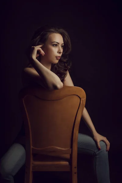 Charming topless woman in blue jeans sitting on a chair — Stock Photo, Image